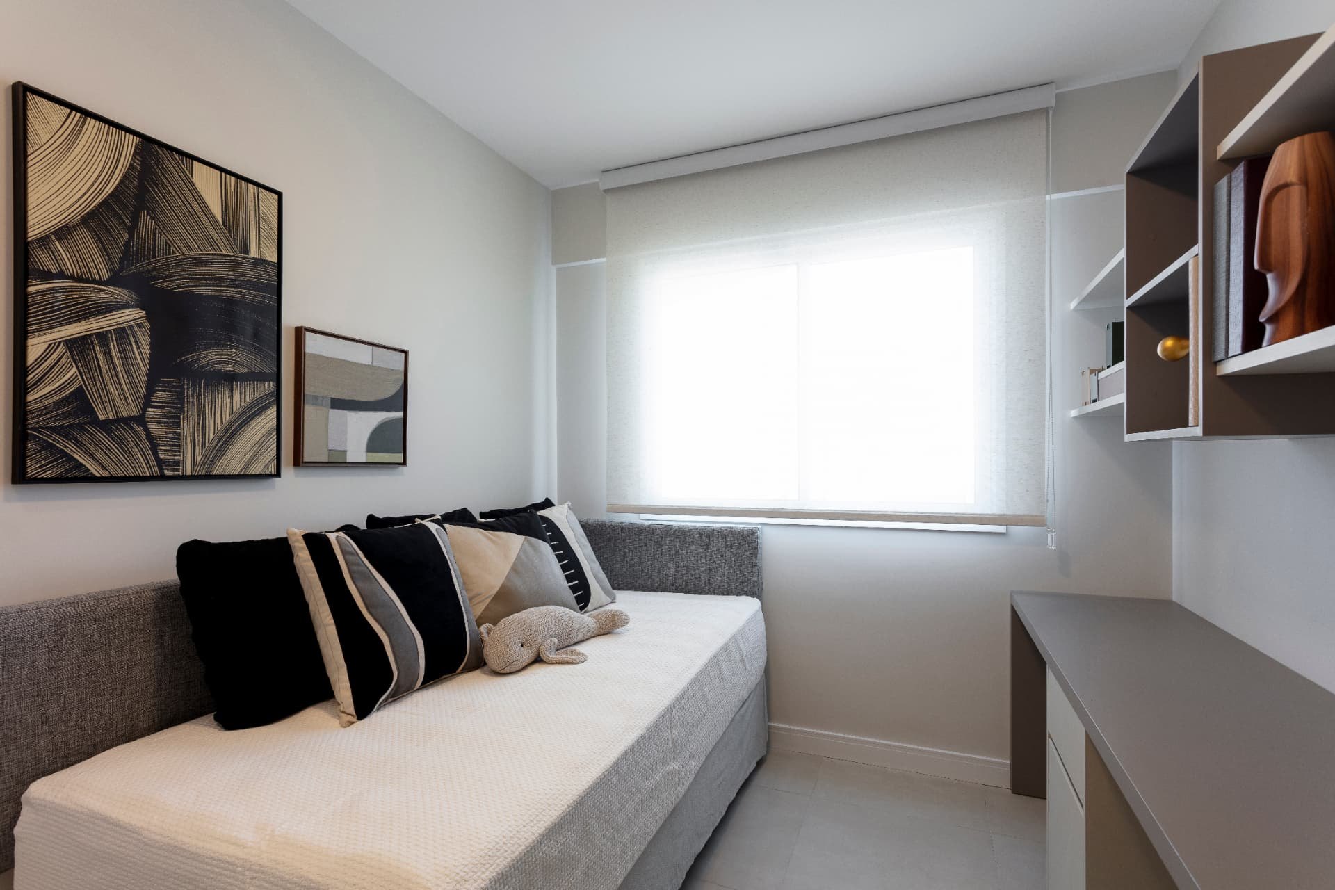 Quarto com cama de solteiro, almofadas em preto e bege e estante
