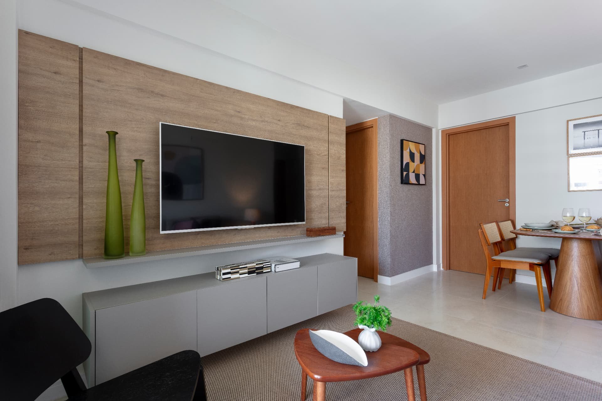 Sala de estar com painel de madeira, rack cinza e mesa de jantar ao fundo